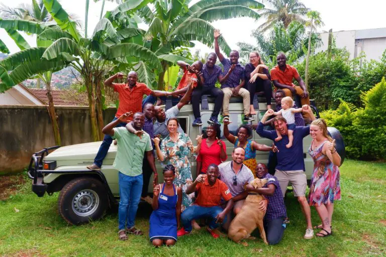 large group of happy staff and guests posing on and around a safari vehicle